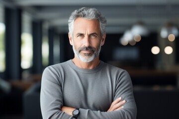 Fototapeta premium Serious middle-aged man with grey hair and beard, crossing his arms confidently.