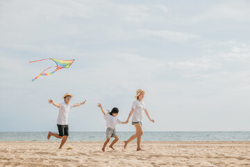 Asian family is flying a kite high in the sky while running on the beach. Happy parents mother and father with their child playing with kite, family is enjoying their time together, summer day