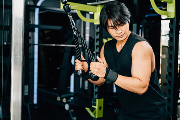 Dark-haired man pulling down on a cable handle to work on his triceps during a strength training...