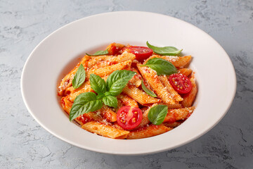 Classic italian pasta penne alla arrabiata with basil and freshly grated parmesan cheese on dark table. Penne pasta with chili sauce arrabbiata.