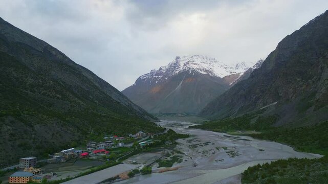 A breathtaking aerial view of Jispa village in Himachal Pradesh, nestled between towering mountains, with a winding river, lush greenery, and vibrant campsites.







