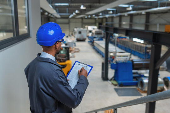 African American man with a blue helmet in a factory unit, an engineer looking at graphs on a tablet checking an automatization process, side view.