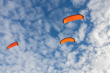 Many silhouettes of red kites in the sky.
Colorful power kites in blue sky. Low angle view of a kite flying. 