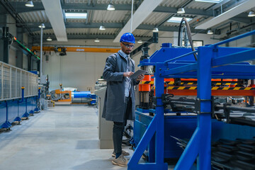 Engineer, with a blue helmet and safety glasses, checking manufacturing machinery, regulating the automatization process on a tablet, close up shot.