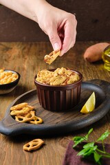 Hummus with sweet potato in a brown ceramic bowl on a brown wooden background. Served with crackers. Chickpea recipes.