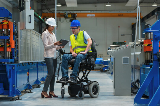 Female manager training a new employee with a disability for a job, explaining work on machines. Industry, inclusion and workplace concept. - Powered by Adobe