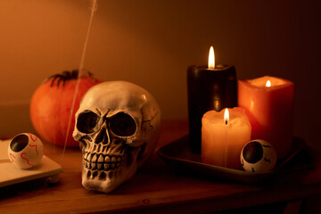 Three burning candles standing on small wooden table next to human skull and eyes, pumpkin with...