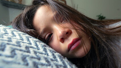 Close-up of a young girl resting her head on a cushion, her expression revealing sadness and fatigue. A poignant moment capturing the depth of childhood emotions