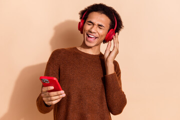 Joyful young man enjoys music with vibrant headphones on a beige background, radiating happiness...