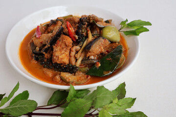 Spicy stir-fried dark water, giant catfish meat, pepper, kaffir lime leaves, purple basil stem and leaves in front of the plate, white background.

