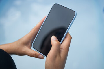 Young woman hand holding a white-screen smartphone mockup, working outdoors on blue background. People and technology concepts. High quality photo