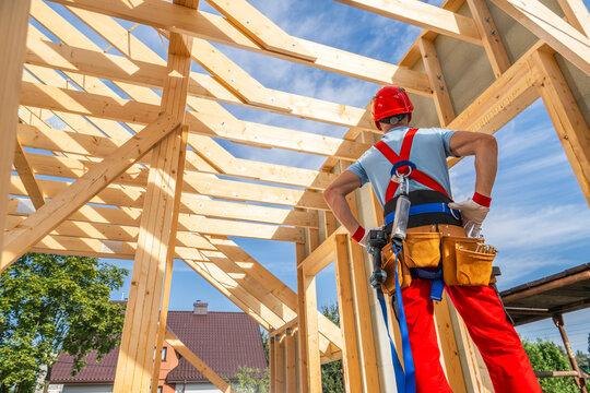 Construction Worker Observes Framing Progress of a New Residential Building on a Sunny Day