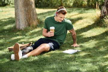 A handsome young man relaxes on the grass, sipping coffee while reading a book, embracing nature...
