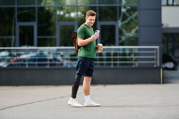 Obraz premium A smiling young man with a prosthetic leg stands outdoors, engaging with his phone and savoring coffee.