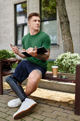 Obraz premium A young man with a disability sits on a bench, enjoying a notebook and coffee in a lively outdoor space.