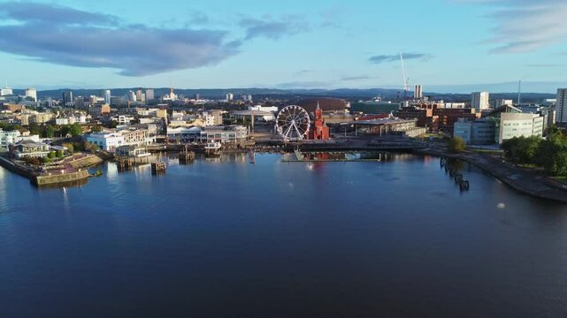 Aerial drone footage of Cardiff Bay area at sunrise, with the Cardiff city centre skyline visible in the distance. Mid altitude parallax, left-to-right tracking shot.