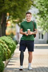 A cheerful man with a prosthetic leg walks confidently outside, sipping coffee and enjoying the day.