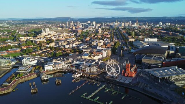 Aerial drone footage of Cardiff Bay area at sunrise, with the Cardiff city centre skyline visible in the distance. High angle left-to-right tracking shot.
