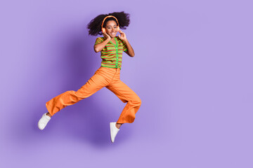 Full length photo of adorable lovely girl wear striped shirt headphones jumping empty space isolated violet color background