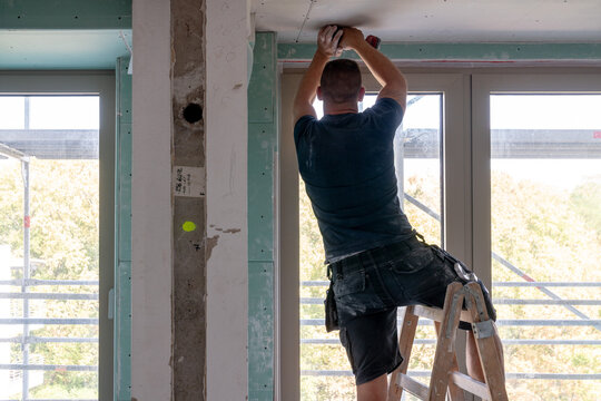 Handwerker auf Leiter bei Deckenmontage in Rohbauwohnung