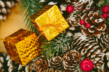 Two small golden gift boxes stacked, set against a blurred background of a festive Christmas wreath.