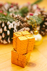 Two small golden gift boxes stacked, set against a blurred background of a festive Christmas wreath.