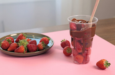 Whole fresh strawberries covered with melted liquid chocolate in cup. Sweet food, dessert on pink...