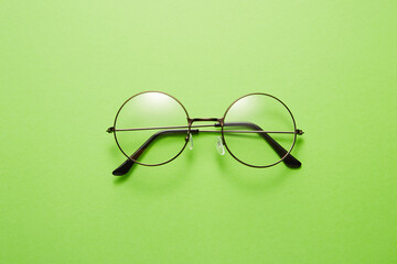 Glasses in round thin metal frame isolated on green surface.