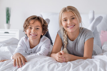 Happy time family concept. Brother and sister lying in bed at the morning and smiling in camera....