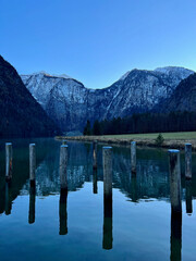 Königssee lake glistens near the port of Saint Bartholomew's Church, framed by a stunning mountain range and lush green fields, creating a picturesque alpine scene in Germany.