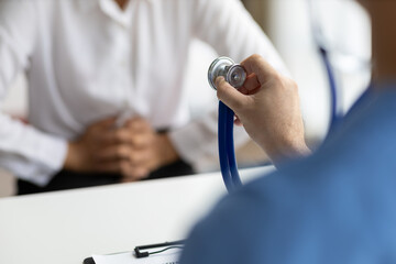 Doctor uses stethoscope to examine body and diagnose disease of female patient in examination room at hospital.