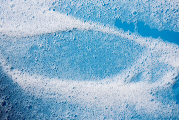 Background and pattern. White soap foam with bubbles, texture on blue tile background.