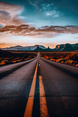 Scenic desert highway at sunset leading towards distant rock formations under a vibrant sky