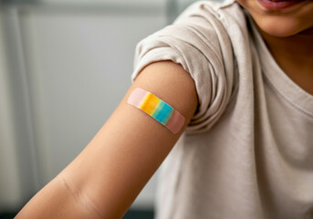 Young child showing off a colorful adhesive bandage applied to their arm after a minor injury in a bright indoor setting