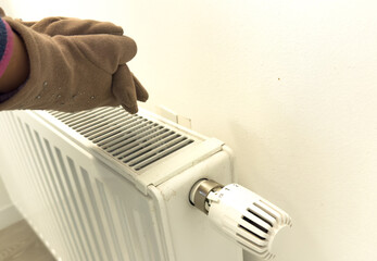 Girl in glove adjusting heating radiator thermostat near white wall, closeup