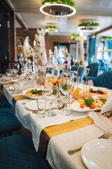 There is a long table set in a cozy restaurant, beautifully adorned with plates, elegantly shaped...