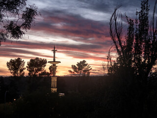 Silhouette of a monument against a vibrant sunset sky with trees in the foreground