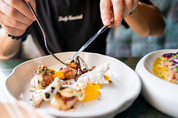 A close-up of a person dining in a restaurant, focusing on their hands cutting a vibrant, gourmet...