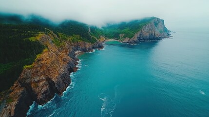 Aerial view of a rugged coastline with green hills and a bay shrouded in fog.