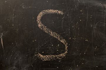 On a black wooden school board, the letter S is written in chalk.