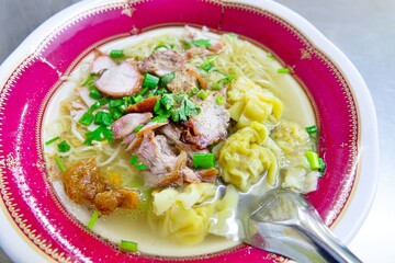 A bowl of soup with noodles and meat in it. The bowl is red and the soup is clear