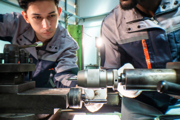 Two focused industrial technicians work together operating heavy machinery in a workshop. The image of teamwork, precision, and technical expertise in an engineering and manufacturing industry