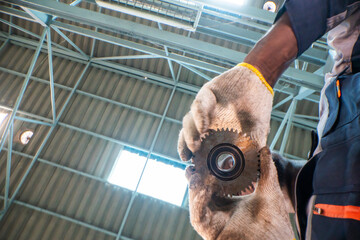 skilled worker inspects an industrial gear while holding it carefully with protective gloves. The...
