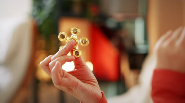 A close-up of a person holding a golden fidget spinner in a relaxed, cozy environment, focusing on stress relief and playful interaction.