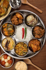 Bengali style thali spread verity cuisine hilsa fish vegetable beef mutton egg curry fry vorta mashed chicken liver sweet yogurt side dish served on rustic metal tin stainless steel plate small bowls
