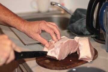 The chef cuts meat with a knife on a wooden board. A man's hand cuts a piece of meat with a knife.