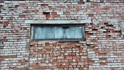 Fototapeta premium a section of an old brick wall with a horizontal rectangular window. The bricks are a mix of red and white, with some areas showing signs of wear and damage, such as missing bricks and uneven surfaces