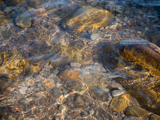 reflections on stones of different sizes piled up on the bottom of the lake under water