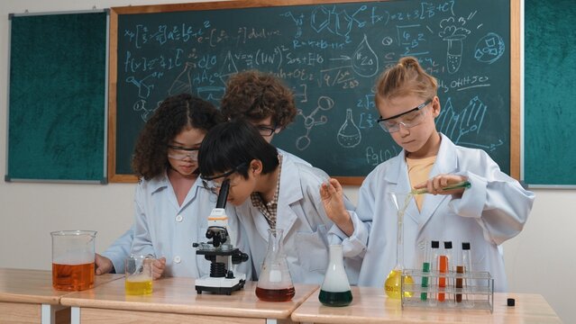 Smart caucasian teacher looking under microscope while diverse children doing experiment at STEM science lesson. Professional happy scientist inspect biochemical example by using microscope. Pedagogy. - Powered by Adobe