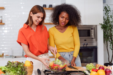 Happy LGBT lesbian couple are cooking together in a kitchen. Straight-haired women wear orange shirts and curly-haired women wear yellow shirts.
